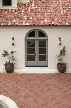 two potted plants on the side of a building with an arched window and tiled roof