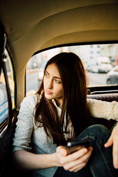 a woman sitting in the back seat of a car looking at her cell phone