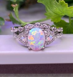 an opal and diamond ring sitting on top of a white surface next to green leaves