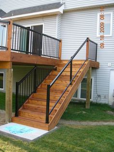 a wooden deck with black railing and handrails next to a white house on the grass