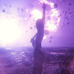 a woman is standing in the water with her arms up to the sky and balloons floating above her