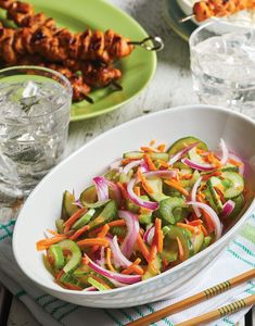 a white bowl filled with veggies on top of a table next to chopsticks