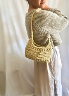 a woman is holding a crocheted handbag in her right hand and looking off to the side