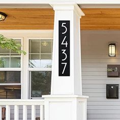 a house number sign sitting on the front porch of a white house with black numbers