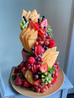 a cake made to look like fruit is sitting on a gold plate with blueberries, strawberries and grapes