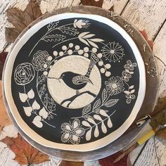 a black and white plate with a bird in the center surrounded by flowers, leaves and acorns