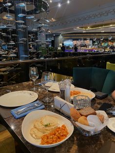 a woman sitting at a table with plates of food in front of her and wine glasses on the side