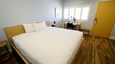 a white bed sitting in a bedroom next to a wooden table and chair on top of a hard wood floor