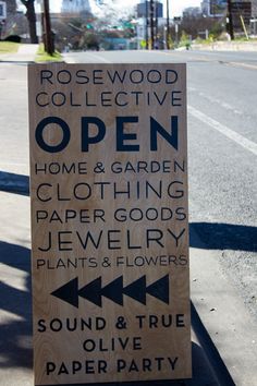 a sign on the side of the road that says rosewood collective open home and garden clothing, paper goods, jewelry, plants & flowers