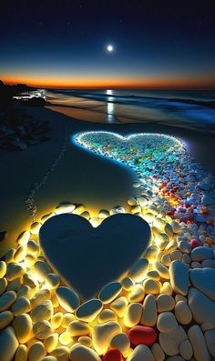 a heart made out of rocks on the beach at night with lights around it and an ocean in the background