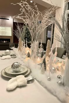 the table is set with silver and white christmas decorations, candles, and snow - covered trees