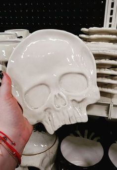 a person holding a white skull shaped plate in front of stacks of plates and bowls