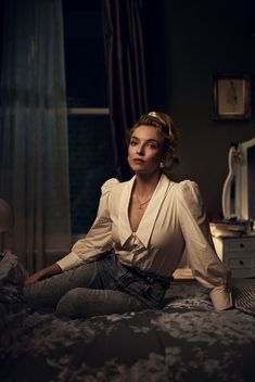 a woman sitting on top of a bed next to a dresser in a dark room