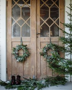 two wreaths hanging on the front door of a house with boots and evergreen branches