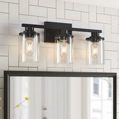 a bathroom vanity with three lights and a mirror on the wall next to it in front of a white tiled wall