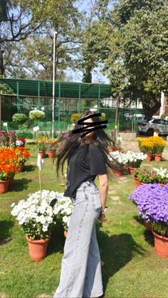 a woman with long hair standing in front of many potted flowers on the grass