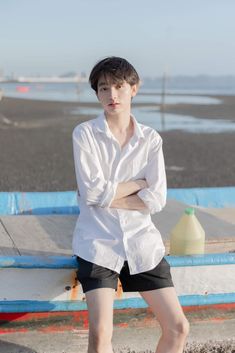 a young man is sitting on a bench by the water with his arms crossed and looking at the camera