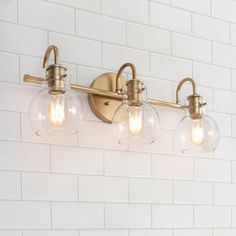 three light bathroom fixture with clear glass globes and brass finish on white brick wall