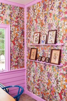 a room with pink walls and flowers on the wall, framed pictures are hung on shelves