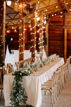 a long table with white linens and greenery is set up for an event