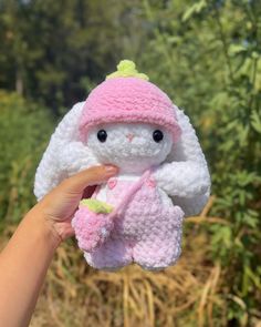 a hand holding a small white and pink stuffed animal