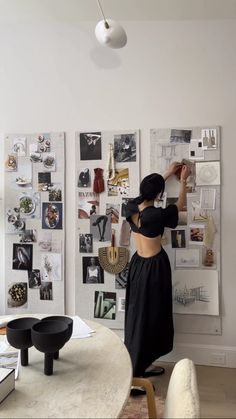 a woman standing in front of a white wall with pictures on the wall behind her