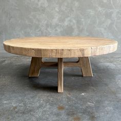 a round wooden table sitting on top of a cement floor next to a gray wall