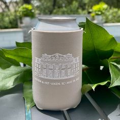 a can cooler sitting on top of a wooden table next to green leafy plants