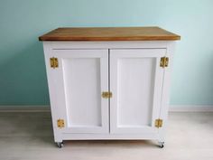 a white cabinet with two doors and a wooden top on casteors in front of a blue wall