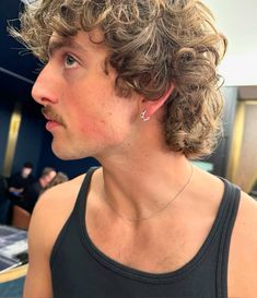 a close up of a person wearing a black tank top with curly hair and piercings