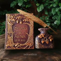 an ornate book with a quill and pen on it sitting next to a vase