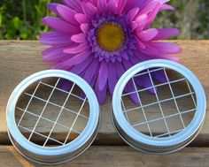 purple flower sitting in front of two metal containers on top of a wooden table next to a fence