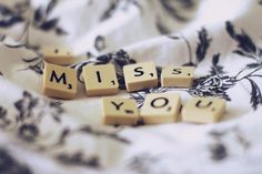 scrabble letters spelling the word miss you on a bed with black and white floral sheets