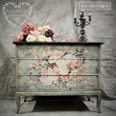 an old dresser with flowers painted on it and a candelabra next to it