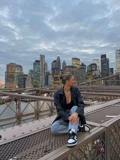 a woman sitting on top of a bridge next to a cityscape with buildings in the background