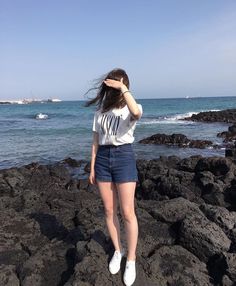 a woman standing on rocks near the ocean