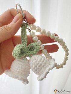 a hand holding a keychain with two bells attached to it and pearls on the end