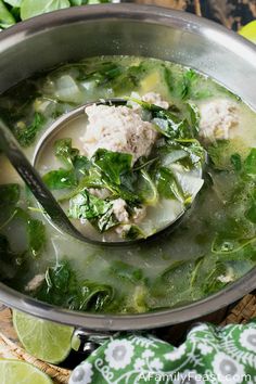 a ladle full of soup with meat and greens on the table next to sliced limes