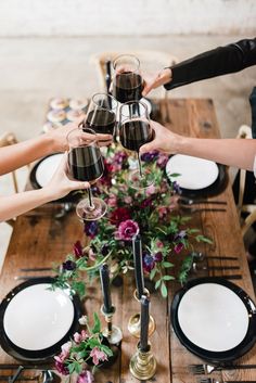 a group of people holding wine glasses over a table with plates and flowers on it