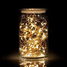 a jar filled with lots of lights sitting on top of a table next to a black background