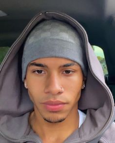 a young man wearing a gray hoodie and earring in the back of a car