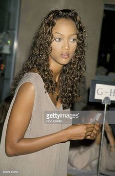 a woman with curly hair standing in front of a microphone and looking at her cell phone