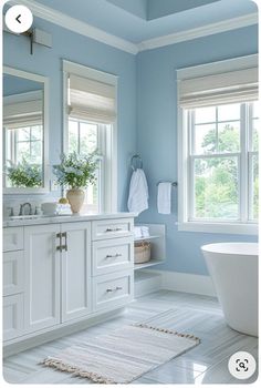 a bathroom with blue walls and white cabinets is shown in this image, there are two windows above the bathtub