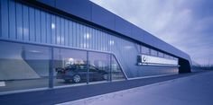 a car is parked in front of a building with large windows that are reflecting the sky