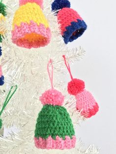 crocheted hats hanging from a white christmas tree with tinsel needles and pom - poms