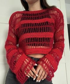 a woman wearing a red knitted sweater and black jeans with her hands in her pockets