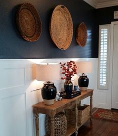 two vases are sitting on a table in front of the wall with three baskets