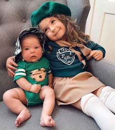 two children are sitting on a couch with their arms around each other and one child is wearing a green hat