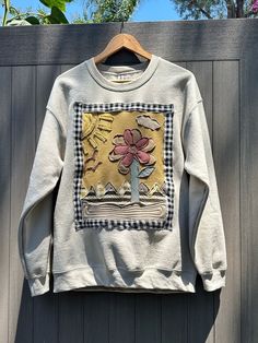 a sweater hanging on a wooden fence with a flower in the center and birds flying around it