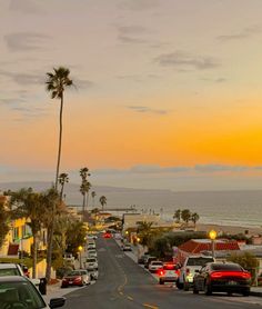 cars are parked on the street in front of some palm trees and buildings at sunset